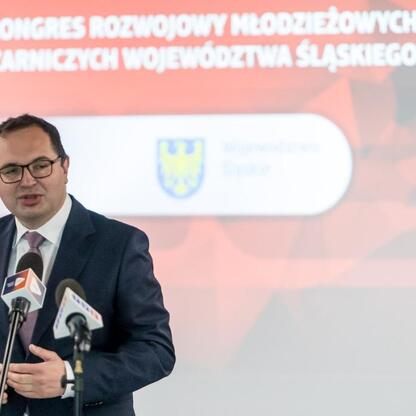 Mężczyzna w garniturze przemawia na podium podczas Kongresu Rozwojowego Młodzieżowych Drużyn Pożarniczych Województwa Śląskiego. (wygenerowano przez AI)