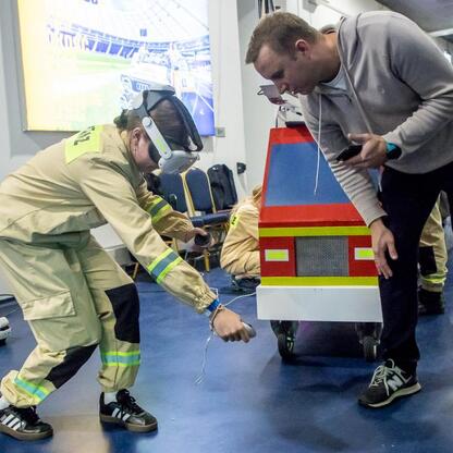 Na zdjęciu przedstawiono moment z trzeciej edycji Kongresu Rozwojowego Młodzieżowych Drużyn Pożarniczych Województwa Śląskiego, zorganizowanego w Superauto.pl Stadium. Strażak demonstruje sprzęt, a uc (wygenerowano przez AI)