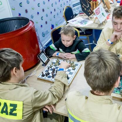 Grupa młodych strażaków uczestniczy w turnieju szachowym podczas Kongresu Rozwojowego Młodzieżowych Drużyn Pożarniczych w Superauto.pl Stadionu Śląskiego. (wygenerowano przez AI)