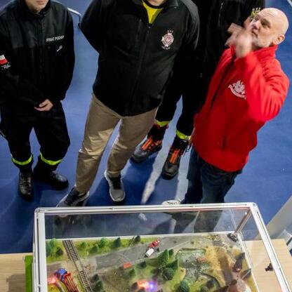 Zebrała się grupa osób, prawdopodobnie strażaków, omawiających dioramę pożarową w konferencji w Superauto.pl Stadion Śląskiego. (wygenerowano przez AI)