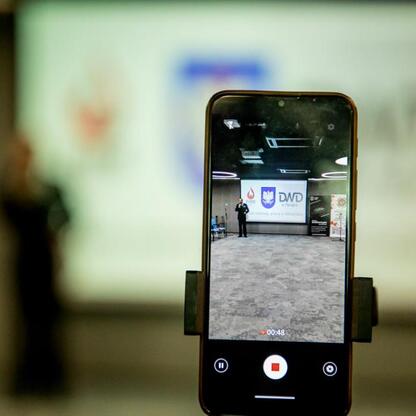 Smartfon nagrywa prezentację na Kongresie Młodzieżowych Drużyn Pożarniczych w Superauto.pl Stadium. (wygenerowano przez AI)