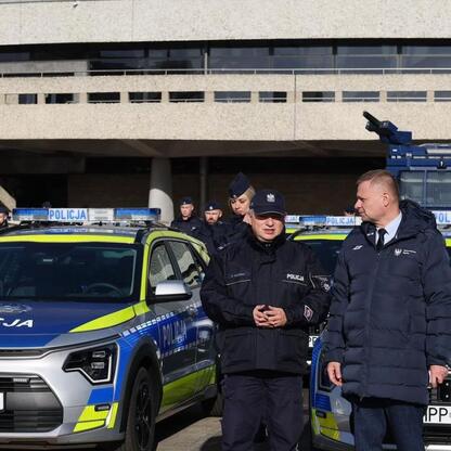Grupa policjantów przed nowoczesnymi hybrydowymi radiowozami Kia Niro Hybrids. (wygenerowano przez AI)