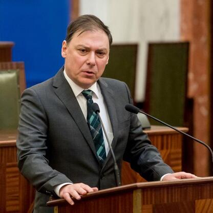 Na podium w sali Sejmu Śląskiego stoi mężczyzna w stroju formalnym, uczestniczący w konferencji o pojednaniu. (wygenerowano przez AI)