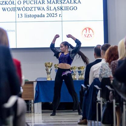 Na zdjęciu młoda sportowczyni z radością podnosi ręce, ciesząc się zwycięstwem w ceremonii wręczenia nagród za Puchar Marszałka Województwa Śląskiego. (wygenerowano przez AI)