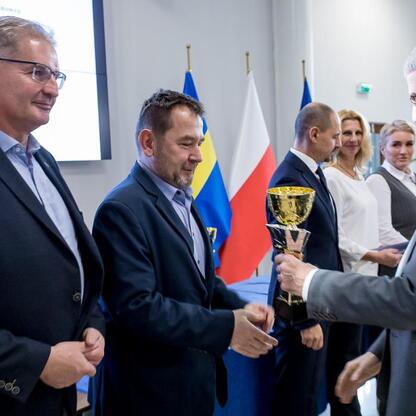 Formalna uroczystość wręczenia nagród w Urzędzie Marszałkowskim w Sosnowcu, gdzie przedstawiciele Sejmiku Województwa Śląskiego prezentują trofea zwycięzcom sportowego konkursu szkół. (wygenerowano przez AI)