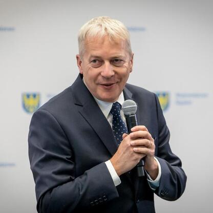 Marszałek Wojciech Saługa prowadzi konferencję prasową na tle logo Województwa Śląskiego i Katowic, omawiając przejęcie kontroli nad Katowice Airport przez województwo. (wygenerowano przez AI)
