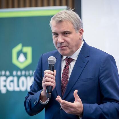 Mężczyzna w niebieskim garniturze i krawacie przemawia do mikrofonu na konferencji prasowej Górnego Śląska Lotniczego Towarzystwa, omawiając przejęcie kontroli nad Katowice Airport przez Województwo Ś (wygenerowano przez AI)