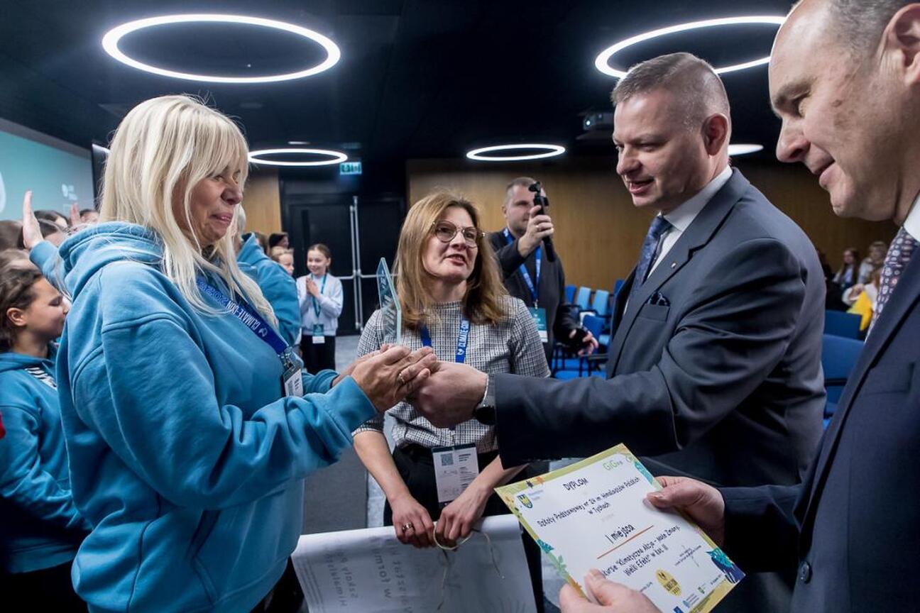 Podczas ceremonii zamknięcia konkursu "Klimatyczna Akcja – Małe Zmiany, Wielki Efekt!" w III Śląskim Konwencie Klimatycznym Climate-Con 2025, dziennikarz rozmawia z uczestniczką. (wygenerowano przez AI)