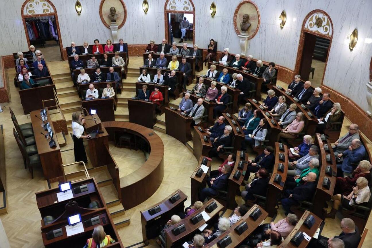 W Silesia Sejm Hall na Śląskim Konwencie Rad Seniorów siedzi uczestniczka, przygotowująca się do wystąpienia. (wygenerowano przez AI)