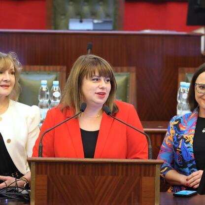 Grupa kobiet w profesjonalnym stroju siedzi przy stole konferencyjnym, dyskutując w formalej sali konferencyjnej. (wygenerowano przez AI)