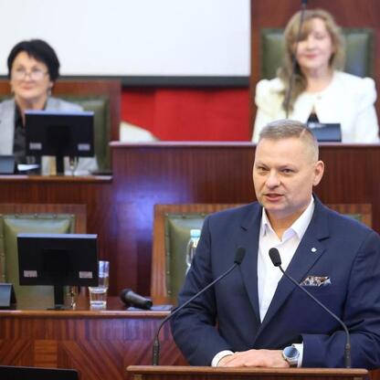 Rafał Adamczyk, członek Zarządu Województwa Śląskiego, przemawia na podium podczas konwentu rad seniorów w Sali Sejmu Śląskiego. (wygenerowano przez AI)