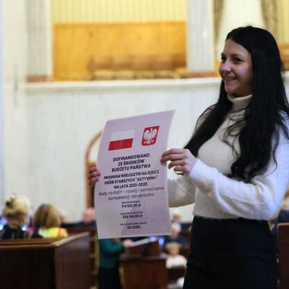 Kobieta prezentuje dokument o finansowaniu i budżecie na konwencji seniorów w Sali Sejmu Śląskiego. (wygenerowano przez AI)