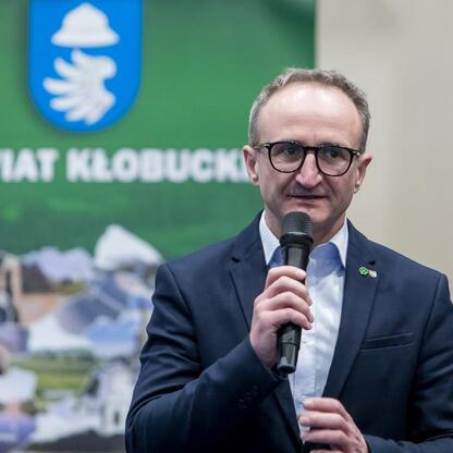 Wicemarszałek Województwa Śląskiego Grzegorz Boski przemawia na spotkaniu w Kłobucku, omawiając postępy w przebudowie dróg i uruchomieniu nowego połączenia kolejowego. (wygenerowano przez AI)