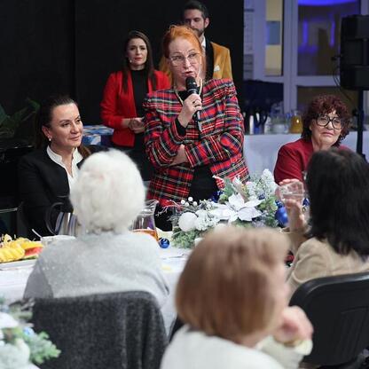 Ostatnie spotkanie Śląskiej Rady Seniorów w Telewizji Katowice. Uczestniczka w czerwonej kurtce przemawia do zgromadzonych. (wygenerowano przez AI)