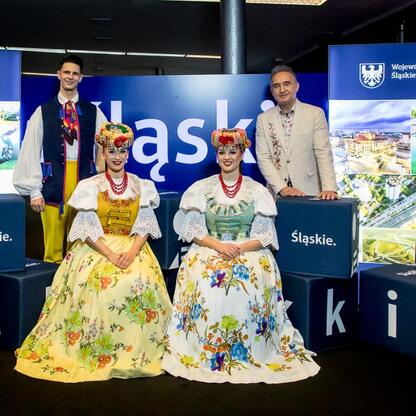 Grupa w tradycyjnych strojach Śląska na tle logo Śląskiego regionu, promującym Nowy Rok w Katowicach. (wygenerowano przez AI)