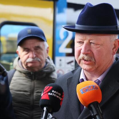 Mężczyzna w czapce i płaszczu przemawia do mikrofonów, podczas testu nowej linii kolejowej Kolei Śląskich. (wygenerowano przez AI)