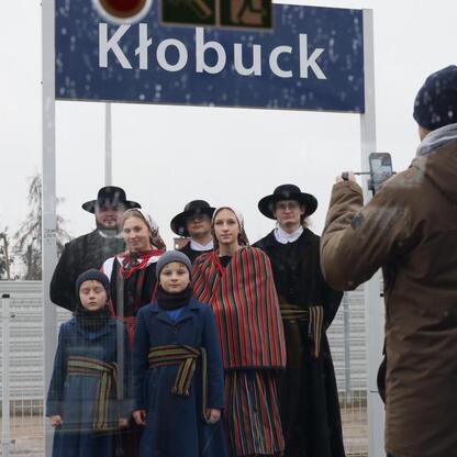 Grupa ludzi w tradycyjnych strojach przedstawiająca Kłobuck, stacja kolejowa, testowy przejazd pociągu Kolei Śląskich. (wygenerowano przez AI)