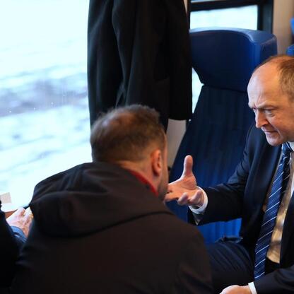 Grupa mężczyzn w strojach formalnych siedzi w pociągu Kolei Śląskich, rozmawiając. (wygenerowano przez AI)