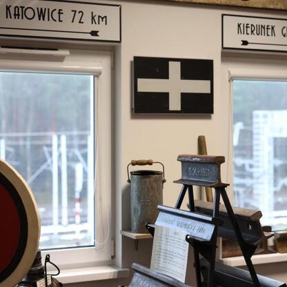 Historia kolejowa w Muzeum Kolei Śląskiej, gdzie eksponowane są urządzenia i znaki informacyjne, wskazujące na Katowice i Gdynię. (wygenerowano przez AI)