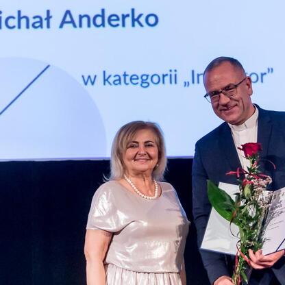 Mężczyzna odbiera nagrodę i bukiet, obok stoi uśmiechnięta kobieta. (wygenerowano przez AI)