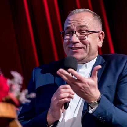 Mężczyzna w ciemnym garniturze i białej koszuli, trzymający mikrofon, podczas uroczystości wręczenia nagród Marszałkowskich w dziedzinie kultury w Katowicach. (wygenerowano przez AI)