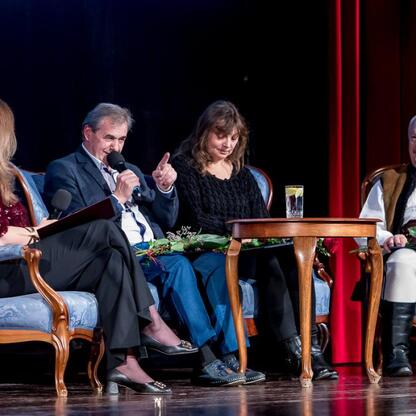 Zdjęcie przedstawia moment z ceremonii wręczenia nagród Marszałka Województwa Śląskiego Culture Awards, która odbyła się w Kinoteatrze Rialto w Katowicach. Czterech uczestników siedzi na ozdobnych krz (wygenerowano przez AI)