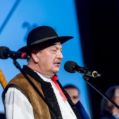 Na zdjęciu: Uczestnik ceremonii wręczenia nagród Marszałka Województwa Śląskiego Culture Awards w tradycyjnym stroju polskim, trzymający instrument, podczas przemówienia. (wygenerowano przez AI)