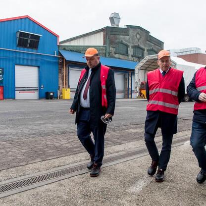 Trzech mężczyzn w kamizelkach ochronnych i hełmach spaceruje po przemysłowej przestrzeni, prawdopodobnie w fabryce Alstom w Chorzowie. (wygenerowano przez AI)
