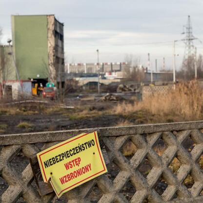 Fotografia przedstawia wyodrębnioną strefę z tablicą ostrzegającą przed niebezpieczeństwem, w tle widoczne są ruiny budynku i linie energetyczne, symbolizujące zakończenie działań związanej z usuwanie (wygenerowano przez AI)