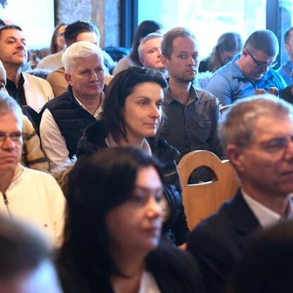 Zdjęcie przedstawia konferencję w Szczyrku, gdzie zgromadzeni ludzie śledzą prezentację. Atmosfera jest profesjonalna i relaksowana. (wygenerowano przez AI)