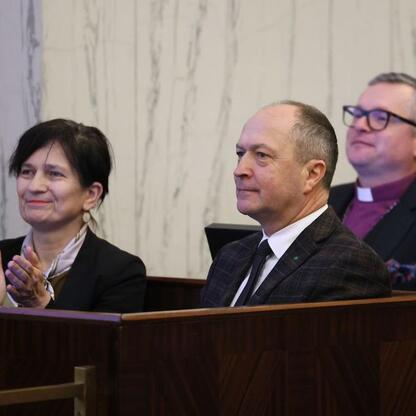 Trzy osoby w strojach formalnych siedzą w sali posiedzeń, podczas sesji Sejmiku Województwa Śląskiego. (wygenerowano przez AI)
