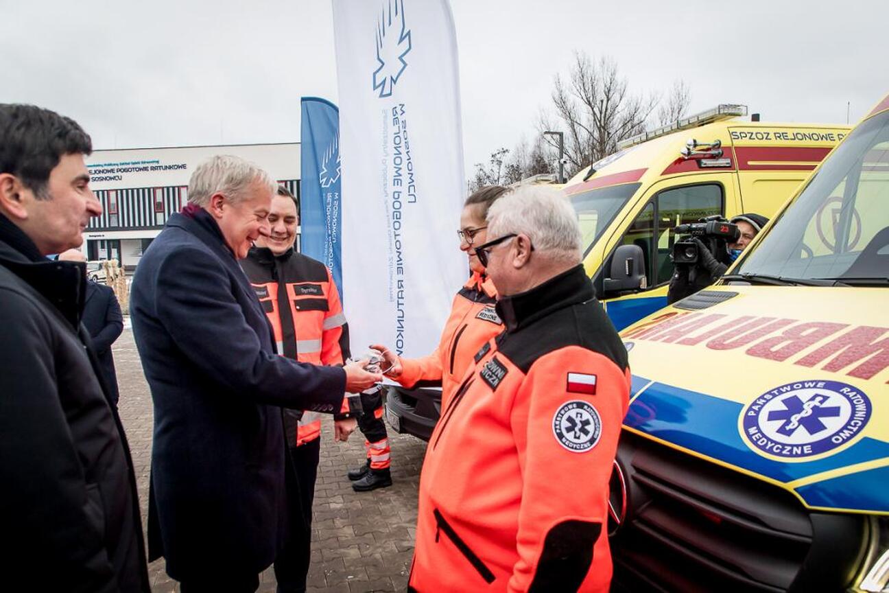 Marszałek Wojciech Saługa i inny mężczyzna w mundurze stoi przed ambulansami, uczestnicząc w uroczystości. (wygenerowano przez AI)