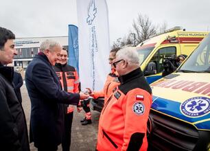 Marszałek Wojciech Saługa i inny mężczyzna w mundurze stoi przed ambulansami, uczestnicząc w uroczystości. (wygenerowano przez AI)