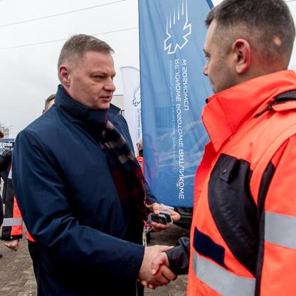 Dwóch pracowników w kamizelkach ochronnych trzyma się za ręce przed sztandarem Sosnowieckiego Pogotowia Ratunkowego. (wygenerowano przez AI)
