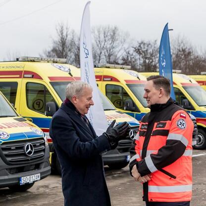 Marszałek Wojciech Saługa i inny mężczyzna w mundurze stoi przed ambulansami, uczestnicząc w uroczystości. (wygenerowano przez AI)