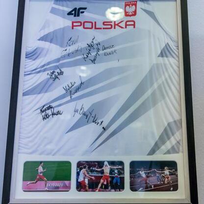 Framed Polish flag shirt with handwritten notes, displayed on an easel in front of a white wall, commemorating the 2020 Tokyo Olympics. (wygenerowano przez AI)