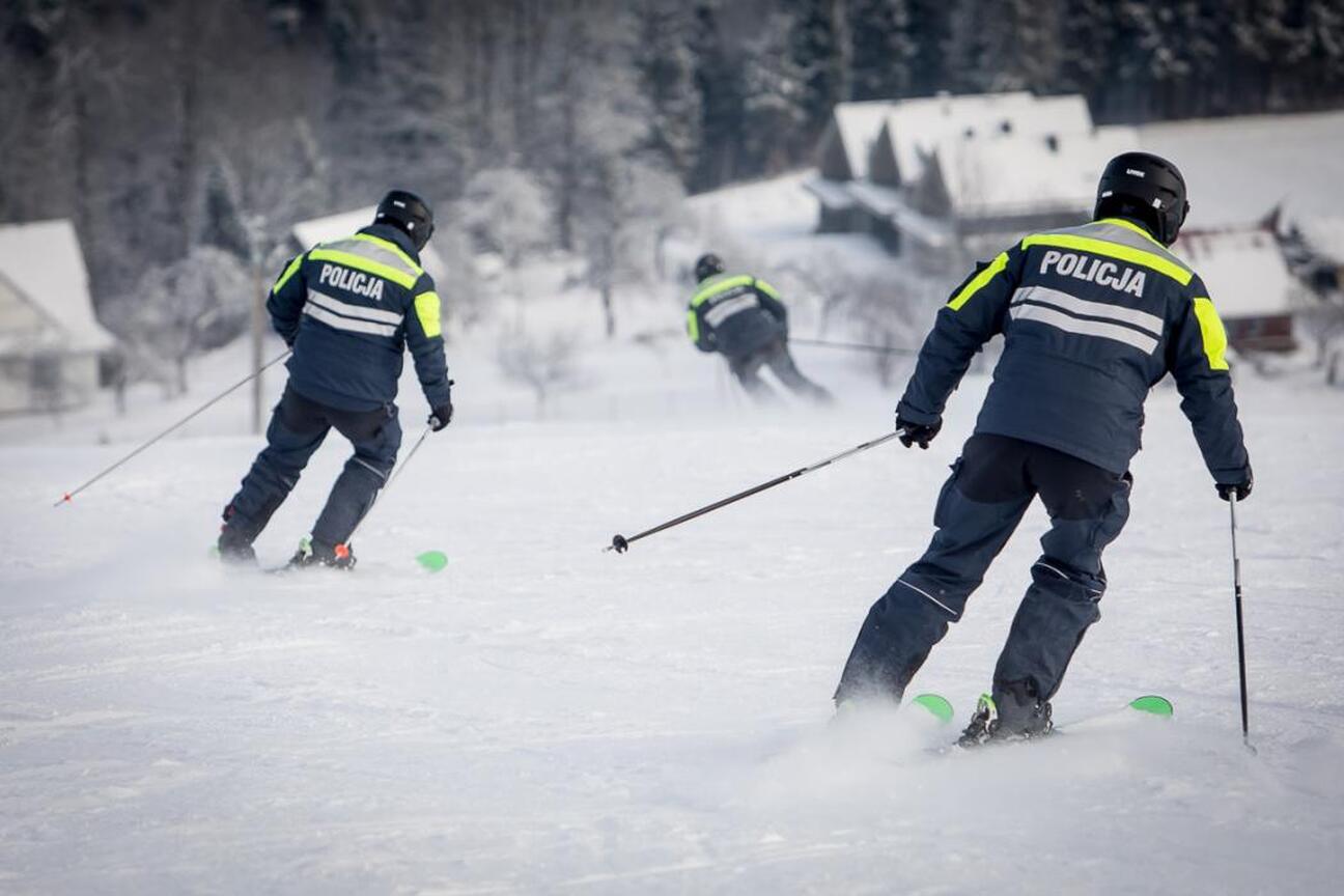 Grupa osób na zimowym wydarzeniu, promującym bezpieczeństwo i odpowiedzialność wśród narciarzy i snowboardzistów. Niebieski namiot z logo policji, czerwone flagi z logiem. (wygenerowano przez AI)