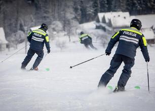 Grupa osób na zimowym wydarzeniu, promującym bezpieczeństwo i odpowiedzialność wśród narciarzy i snowboardzistów. Niebieski namiot z logo policji, czerwone flagi z logiem. (wygenerowano przez AI)