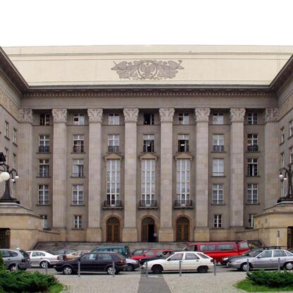 Widoczna jest wielopoziomowa budowla z wieloma oknami i płaskim dachem, przedstawiająca widok na parking z samochodami. (wygenerowano przez AI)