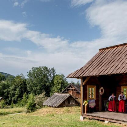 Dwie kobiety w tradycyjnych strojach folkowych stoją na drewnianej platformie, uczestnicząc w wydarzeniu kulturalnym. (wygenerowano przez AI)