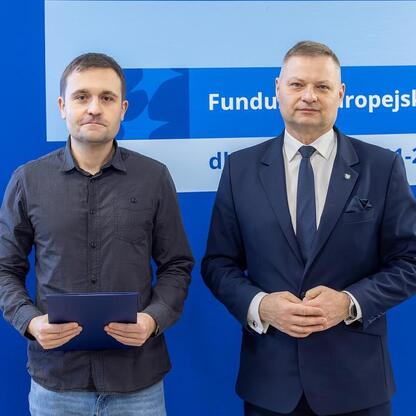 Dwóch mężczyzn przed logo Funduszy Europejskich dla Śląska 2021-2027. (wygenerowano przez AI)