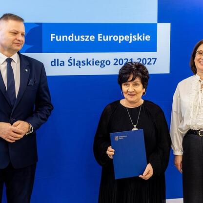Trzech ludzi w profesjonalnym stroju stoi przed niebieskim tłem z napisem 