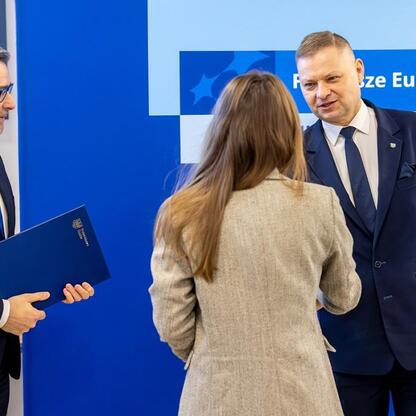 Trzech oficjalnych przedstawicieli stoi przed napisem 