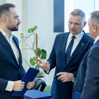 Trzech mężczyzn w formalnym ubiorze dyskutuje w biurze, omawiając projekt finansowany z funduszy europejskich dla przedszkoli w Śląskim. (wygenerowano przez AI)