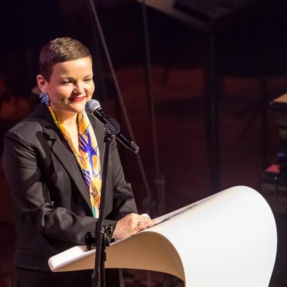 Podczas inauguracji Bielska-Białej jako Polskiej Stolicy Kultury, kobieta w czarnej sukni i kolorowym szaliku przemawia na podium. (wygenerowano przez AI)