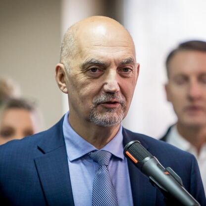 Mężczyzna w garniturze przemawia do mikrofonu, podczas konferencji prasowej w Jaworznie, dotyczącej inwestycji w ochronę ludności i bezpieczeństwo publiczne. (wygenerowano przez AI)