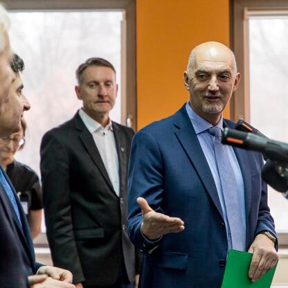 Mężczyzna w garniturze przemawia na konferencji prasowej, wskazując na mikrofony, w tle widoczne logo Województwa Śląskiego. (wygenerowano przez AI)