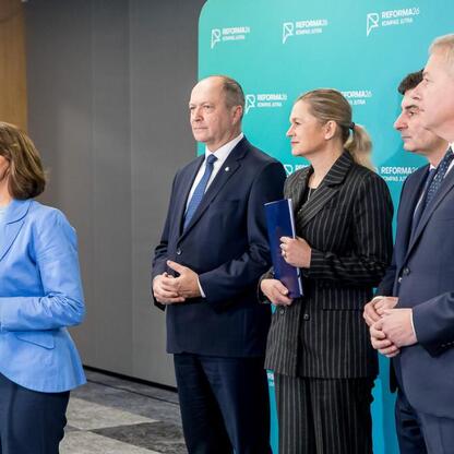 Grupa osób w niebieskich garniturach i żółtych kamizelkach omawia reformę edukacji podczas konferencji w Sosnowcu. (wygenerowano przez AI)