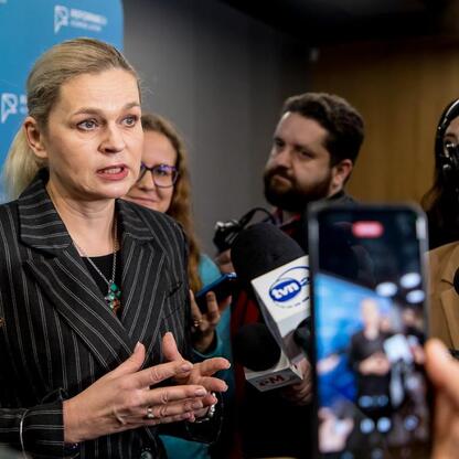 Widoczna na zdjęciu kobieta w czarno-białym paskowanym płaszczu przemawia w sali konferencyjnej na Stadionie Śląskim, związana z reformą edukacji 