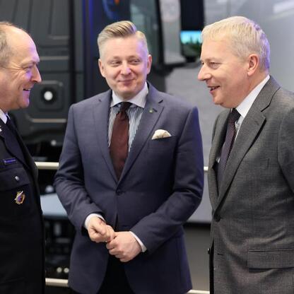 Trzech mężczyzn w strojach formalnych rozmawiających w profesjonalnym środowisku, związany z bezpieczeństwem ruchu drogowego w Katowicach. (wygenerowano przez AI)
